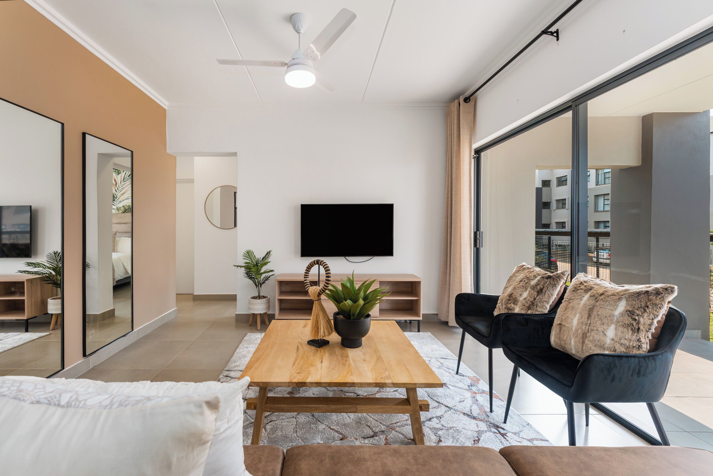 Een moderne woonkamer met een houten salontafel, een zwarte bank en een flatscreen televisie die aan de muur is bevestigd.