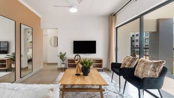 Een moderne woonkamer met een houten salontafel, een zwarte bank en een flatscreen televisie die aan de muur is bevestigd.