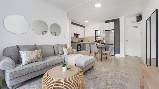 A modern living room with a grey sofa, a round coffee table, and a kitchen in the background. - Ballito Village Estate (Ballito)