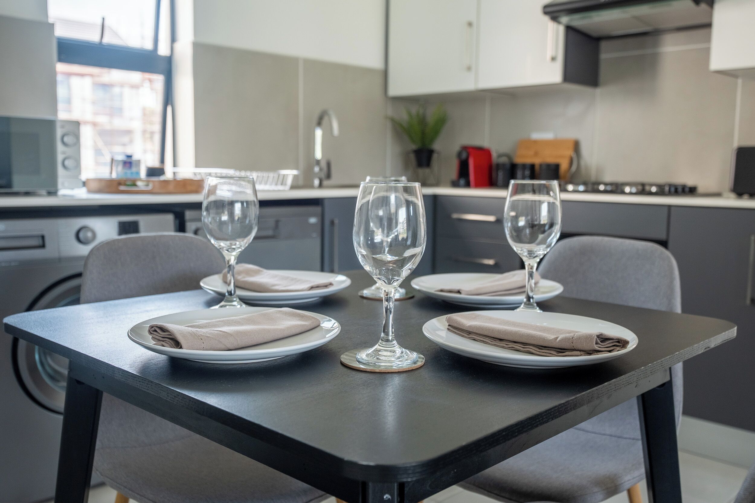 Una cucina moderna con un tavolo da pranzo apparecchiato per quattro, inclusi bicchieri da vino e tovaglioli piegati.