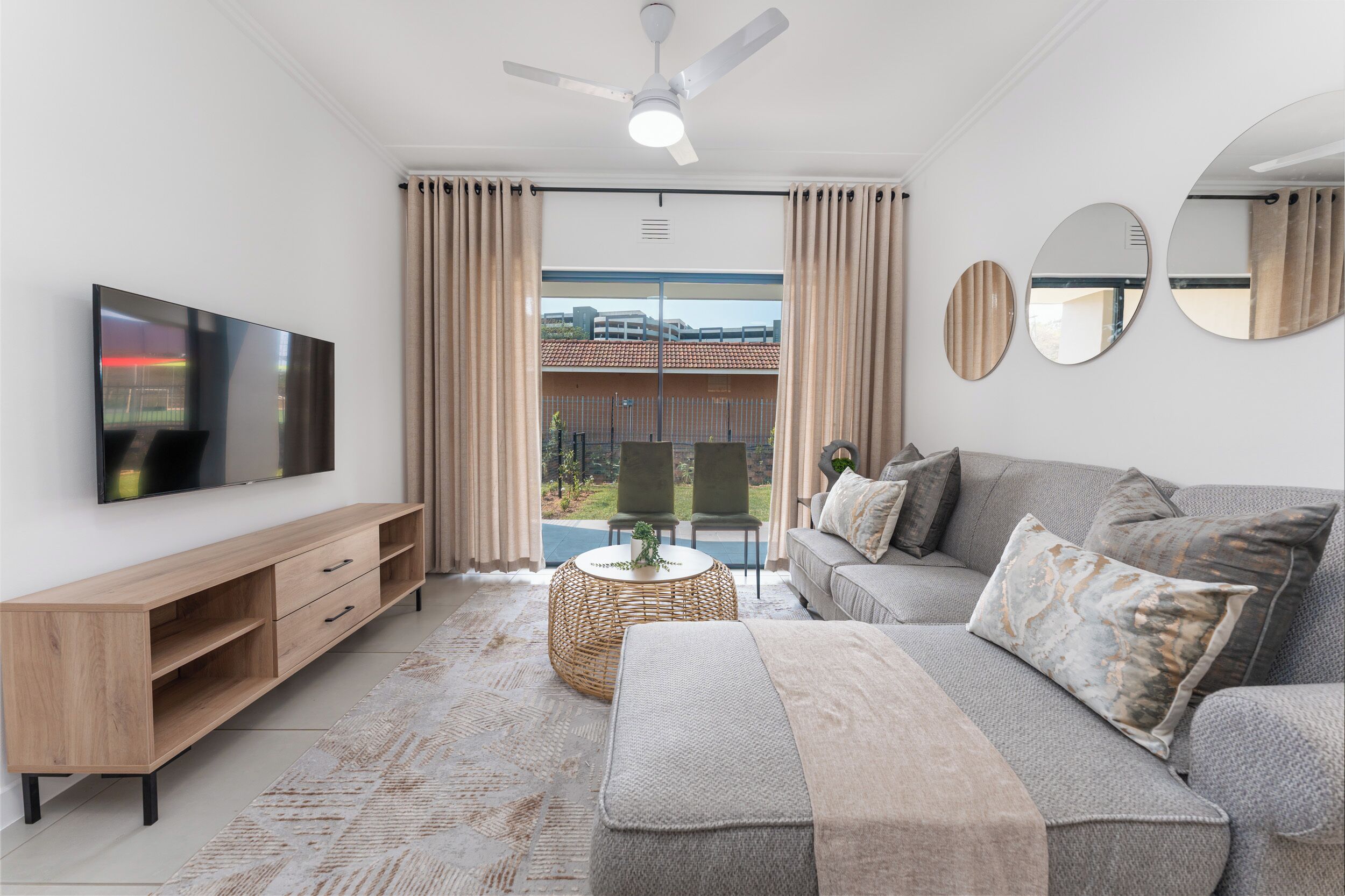 A modern living room with a flat-screen TV, a sofa, a coffee table, and a balcony with curtains.