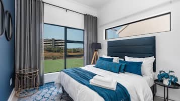 A bedroom with a large bed, a view of a tennis court, and a modern design.