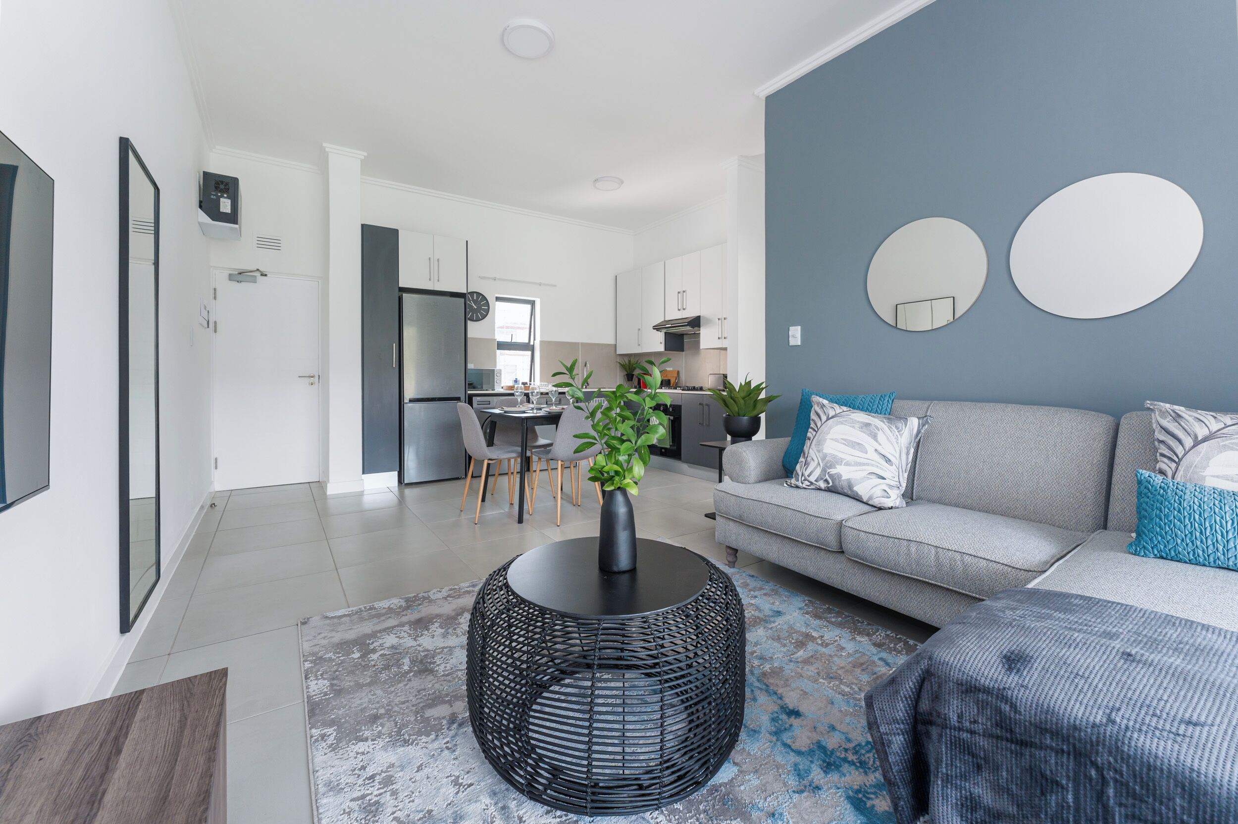 Een moderne woonkamer met een grijze bank, een ronde zwarte salontafel, en een eethoek met een tafel en stoelen.
