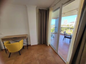 Ein Balkon mit Stuhl und Tisch, eine Schiebetür und Blick auf Gebäude und Grünflächen.