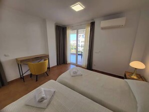 Ein Hotelzimmer mit zwei Betten, einem Schreibtisch, einem Stuhl, einer Lampe und Blick ins Freie.