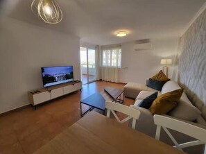 Ein Wohnzimmer mit Fernseher, einer Couch, einem Couchtisch und einem Esstisch.