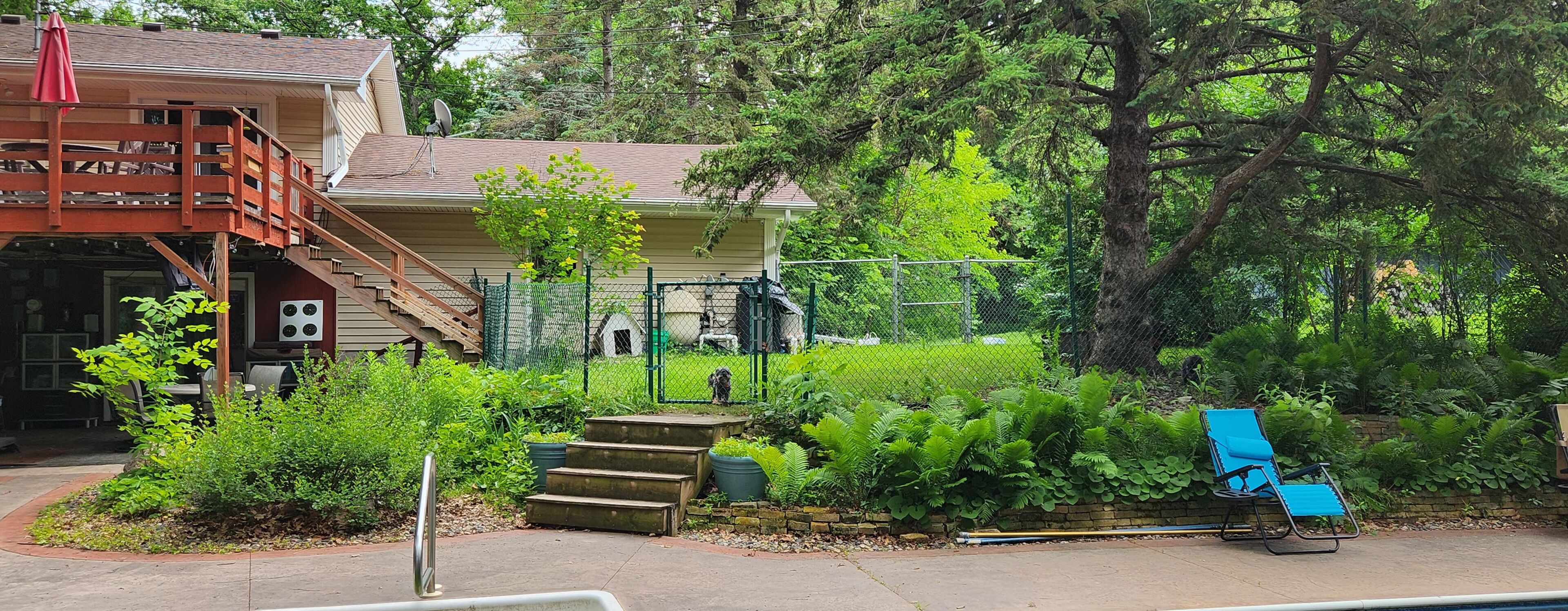 A two-story house with a fenced yard, a dog, and a blue chair.