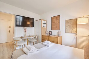Ein Hotelzimmer mit einem Bett, einem Schreibtisch, einem Sessel, einem Fernseher, einer Holzkommode und einer Wandleuchte.