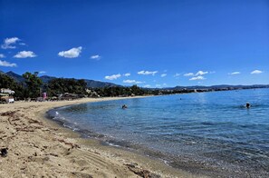Uma praia com águas cristalinas, areal arenoso e montanhas ao fundo.