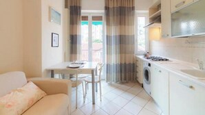 En kompakt bolig med spiseplads, sofa, vaskemaskine og tekøkken.