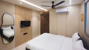 A modern hotel room with a bed, a ceiling fan, a mounted TV, and a large mirror. - Nirrtul Sapphire Studio Apartment Specious Cozy & Quite (Surat)