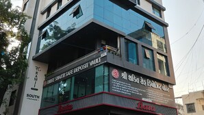 A multi-story building with a modern architectural design, featuring a glass facade and a storefront with a sign for a shoe store. - Nirrtul Sapphire Studio Apartment Specious Cozy & Quite (Surat)
