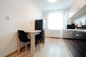 Une petite cuisine avec une table à manger, deux chaises, un réfrigérateur et une fenêtre.