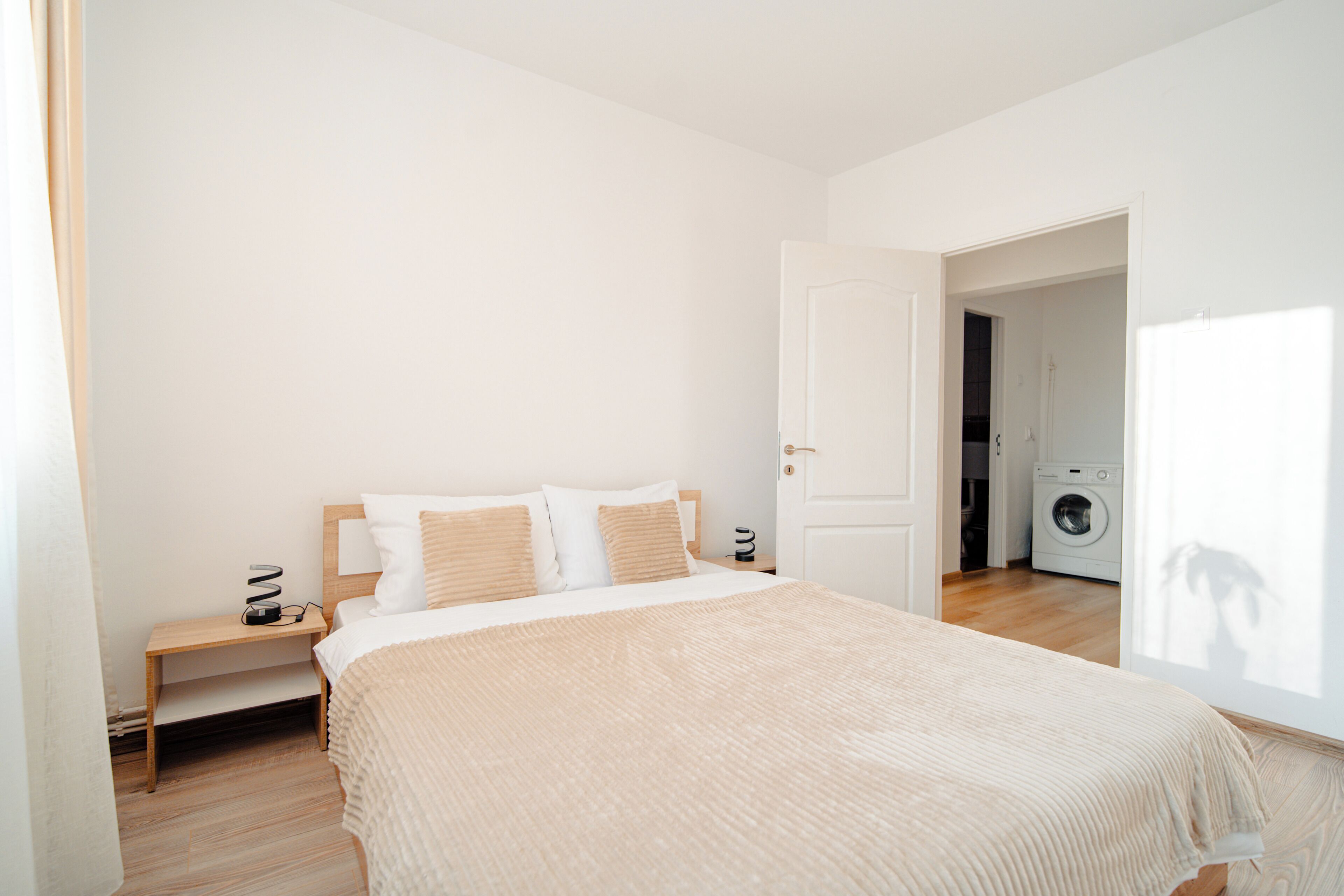 Een slaapkamer met een bed, nachtkastje en een deur naar een wasserij.