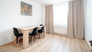 A dining area with a wooden table, black chairs, a painting on the wall, and a large window with curtains.