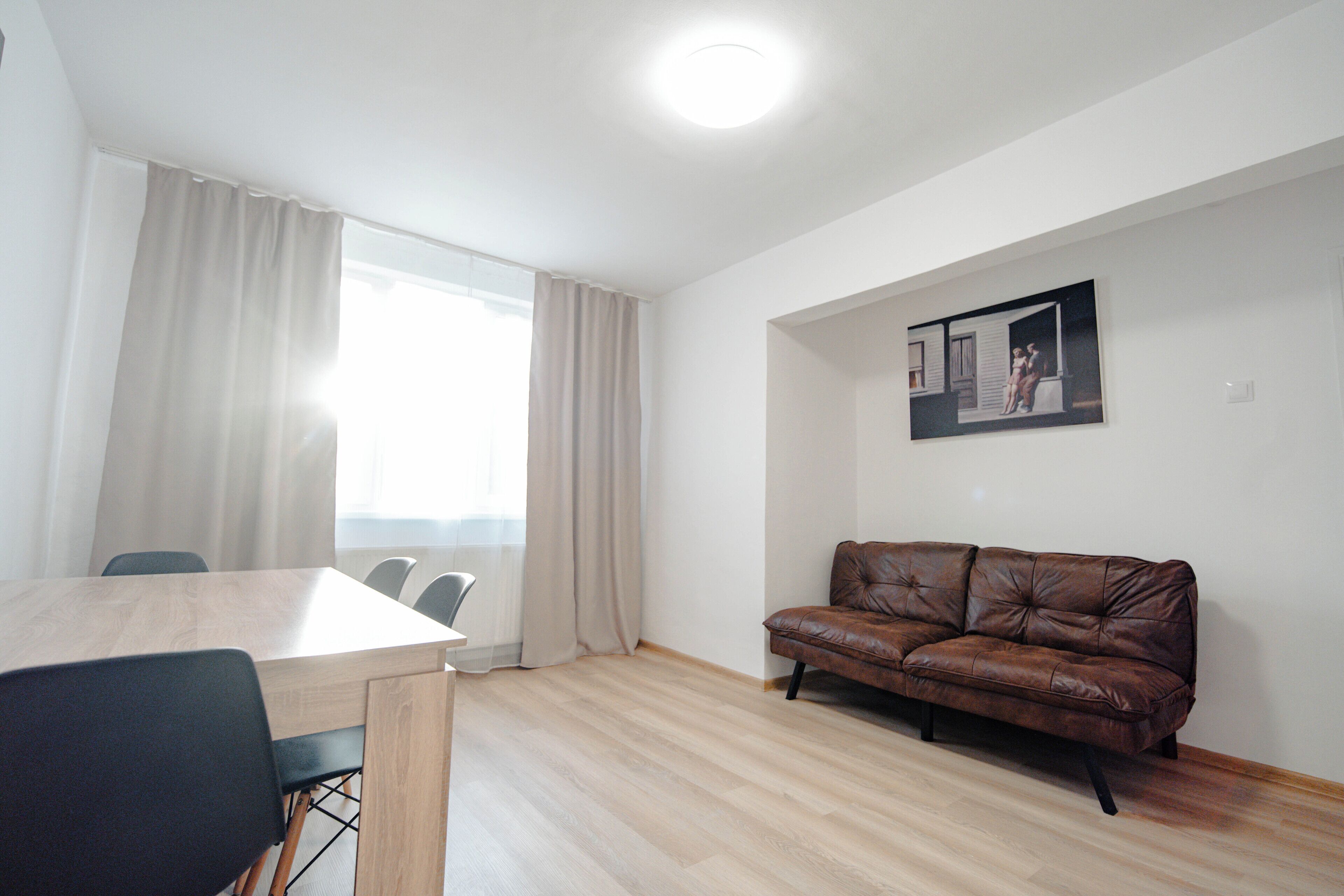 A room with a wooden dining table, chairs, a brown leather sofa, and a framed picture on the wall.