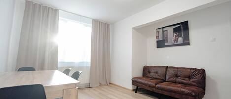 A room with a wooden dining table, chairs, a brown leather sofa, and a framed picture on the wall.