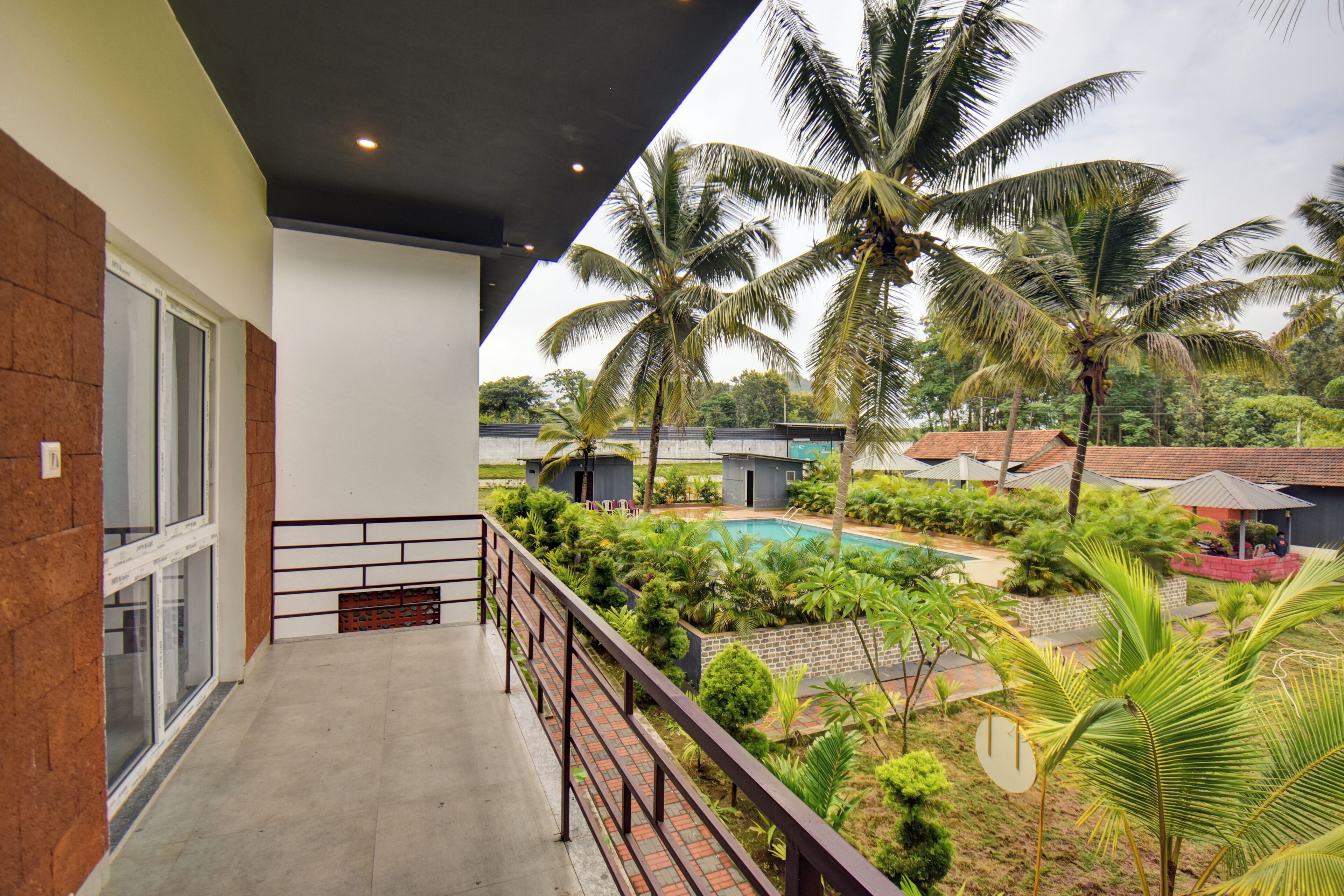 A balcony with a view of a swimming pool, palm trees, and a brick building.