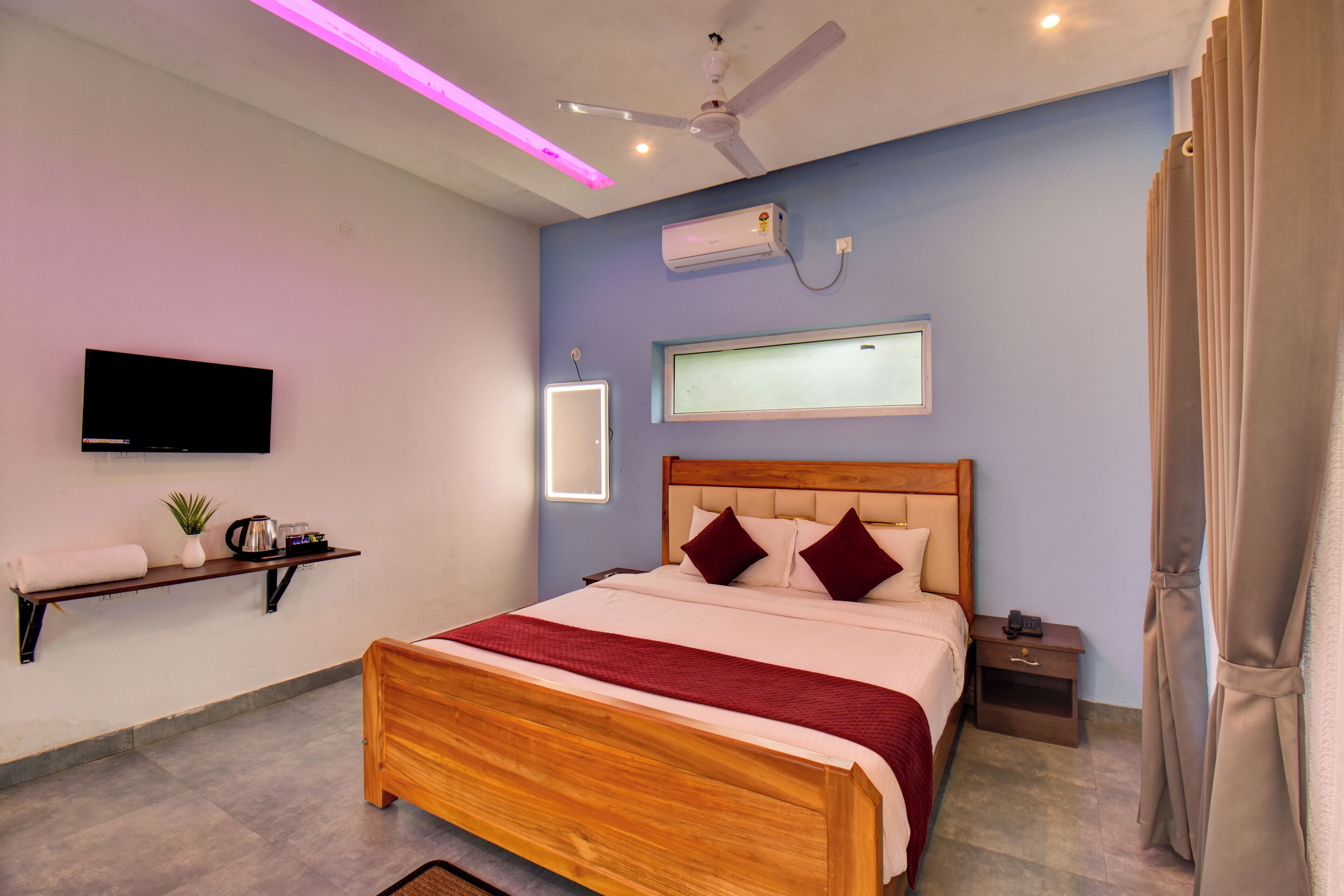 Une chambre moderne avec un lit en bois, une table de chevet, une commode, un téléviseur fixé au mur, un ventilateur de plafond et une fenêtre donnant sur un beau paysage.