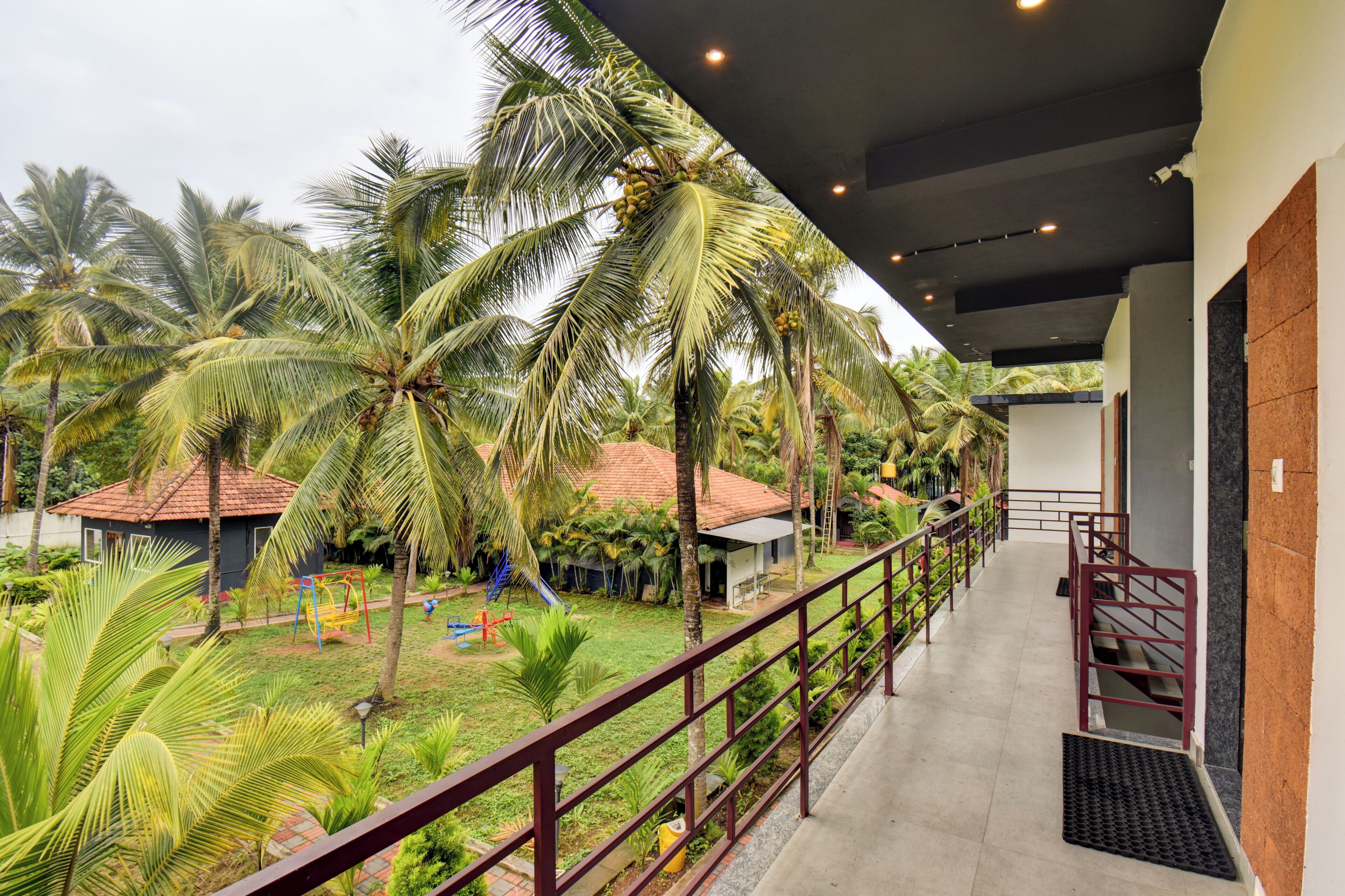 Un balcón con vistas a un jardín tropical, que incluye palmeras y una zona de juegos infantiles.