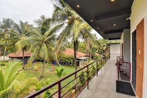 A balcony with a view of a tropical garden, including palm trees and a children's play area. - Orange Vista Resort Coorg (Kushalnagar)