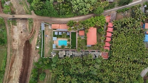 An aerial view of a resort with a swimming pool, palm trees, and a road.