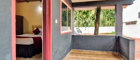 A room with a bed, a small table, and a view of palm trees through a window.
