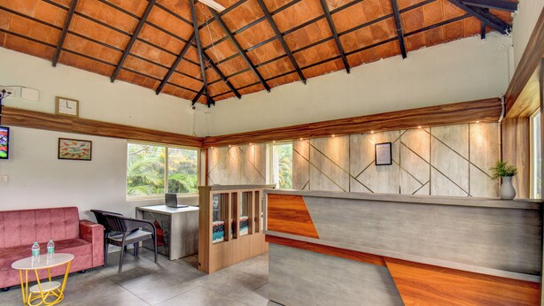 Un interior moderno con techo de madera, un sofá, un escritorio y vistas al exterior con vegetación.