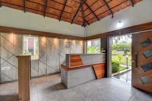 A reception desk with a wooden finish, a tiled floor, and a ceiling with a patterned design. - Orange Vista Resort Coorg (Kushalnagar)