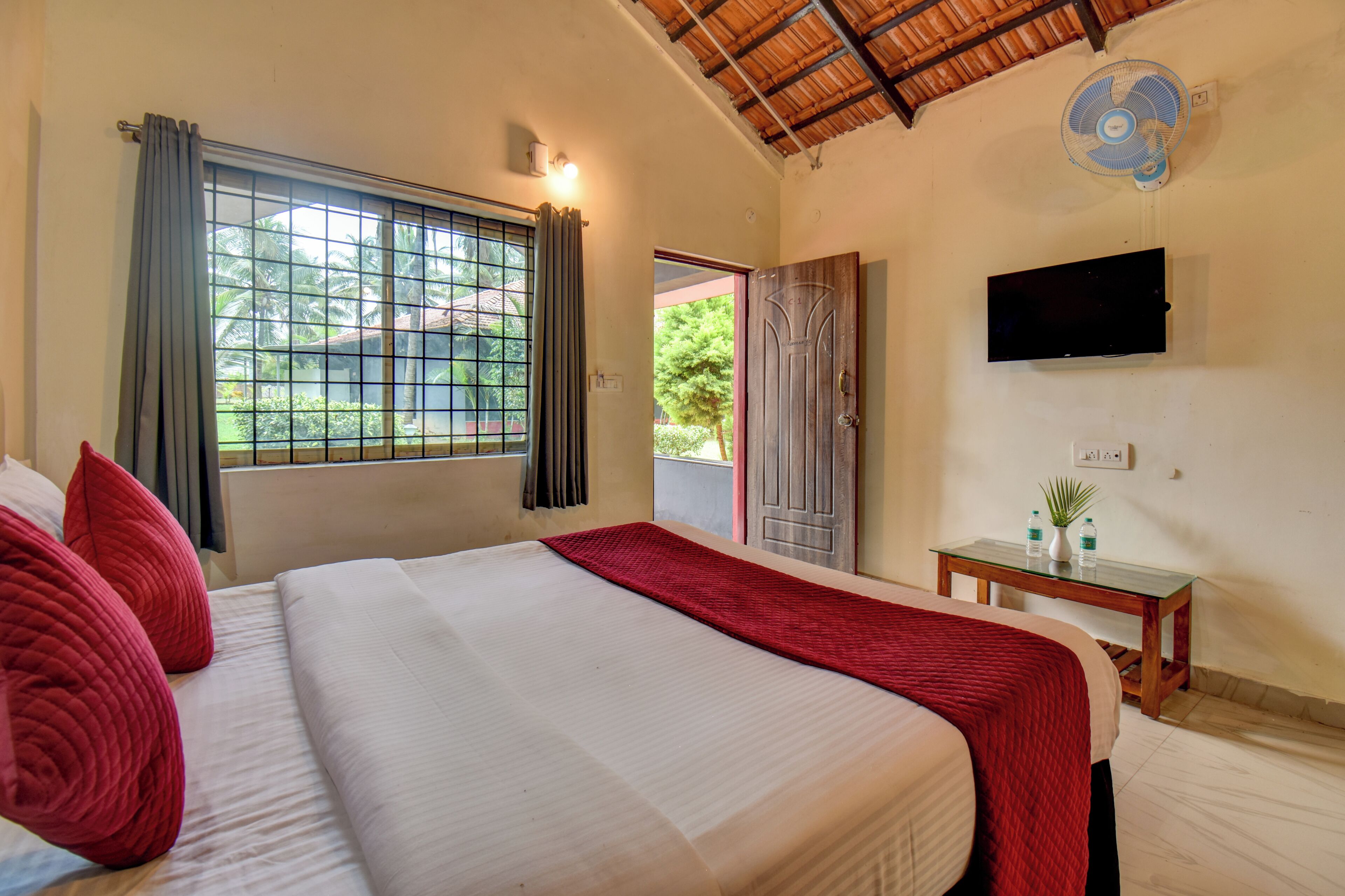 Habitación de hotel con cama, televisión montada en la pared, una mesita con una planta y una ventana con cortinas.