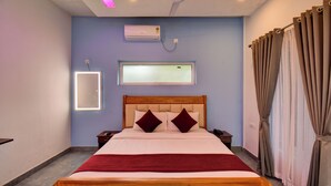 Habitación de hotel con cama, mesita de noche, ventilador de techo, unidad de aire acondicionado, espejo en la pared y ventana con cortinas.