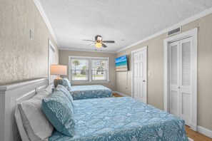 Ein Schlafzimmer mit zwei Betten, einem Deckenventilator, einem Fernseher und einem Fenster mit Jalousien.