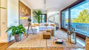 Ein modernes Wohnzimmer mit einem weißen Sofa, einer großen Topfpflanze, einem Stativ und einer Wendeltreppe.