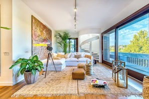 Ein modernes Wohnzimmer mit einem weißen Sofa, einer großen Topfpflanze, einem Stativ und einer Wendeltreppe.