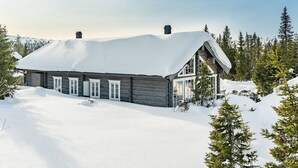 Una cabaña de troncos con techo cubierto de nieve, rodeada de árboles y paisajes nevados.