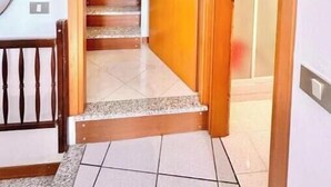 Une porte en bois qui donne sur un escalier dont le sol est recouvert de carreaux.