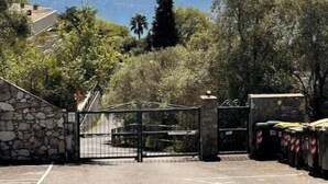 Une allée pavée mène à une entrée fermée par un portail, d’où l’on peut admirer la vue sur l’océan.