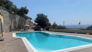 Une piscine rectangulaire avec un mur en pierre et un drapeau sur une terrasse aménagée sur le toit.