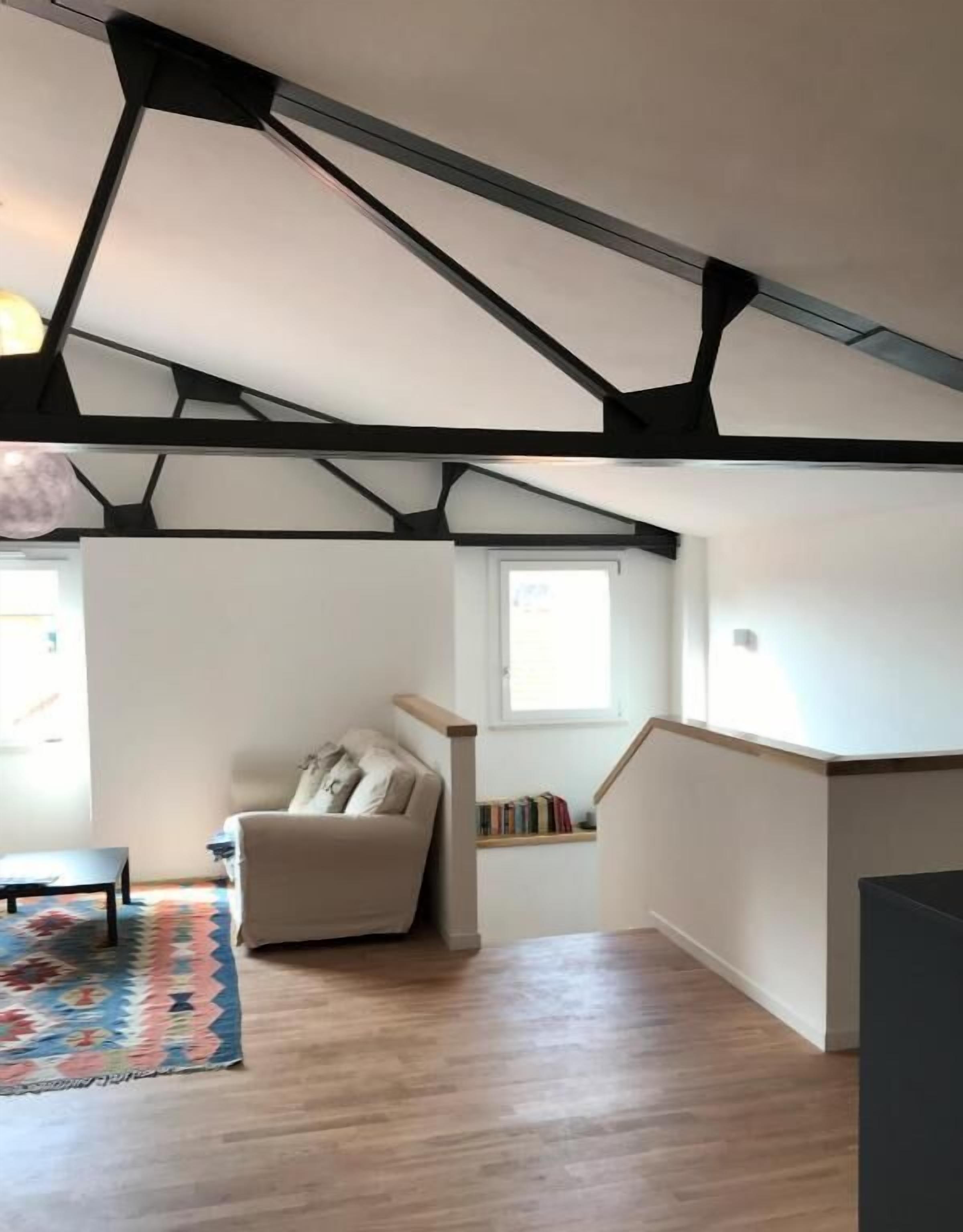 A modern loft-style living space with exposed beams, a sofa, a small table, and a patterned rug.