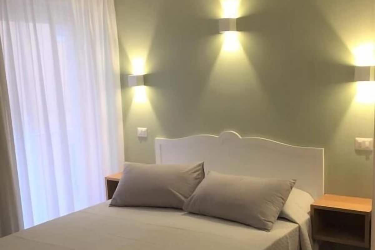 Una cama con cabecera blanca, dos mesitas de noche y una pared verde claro con luces empotradas.