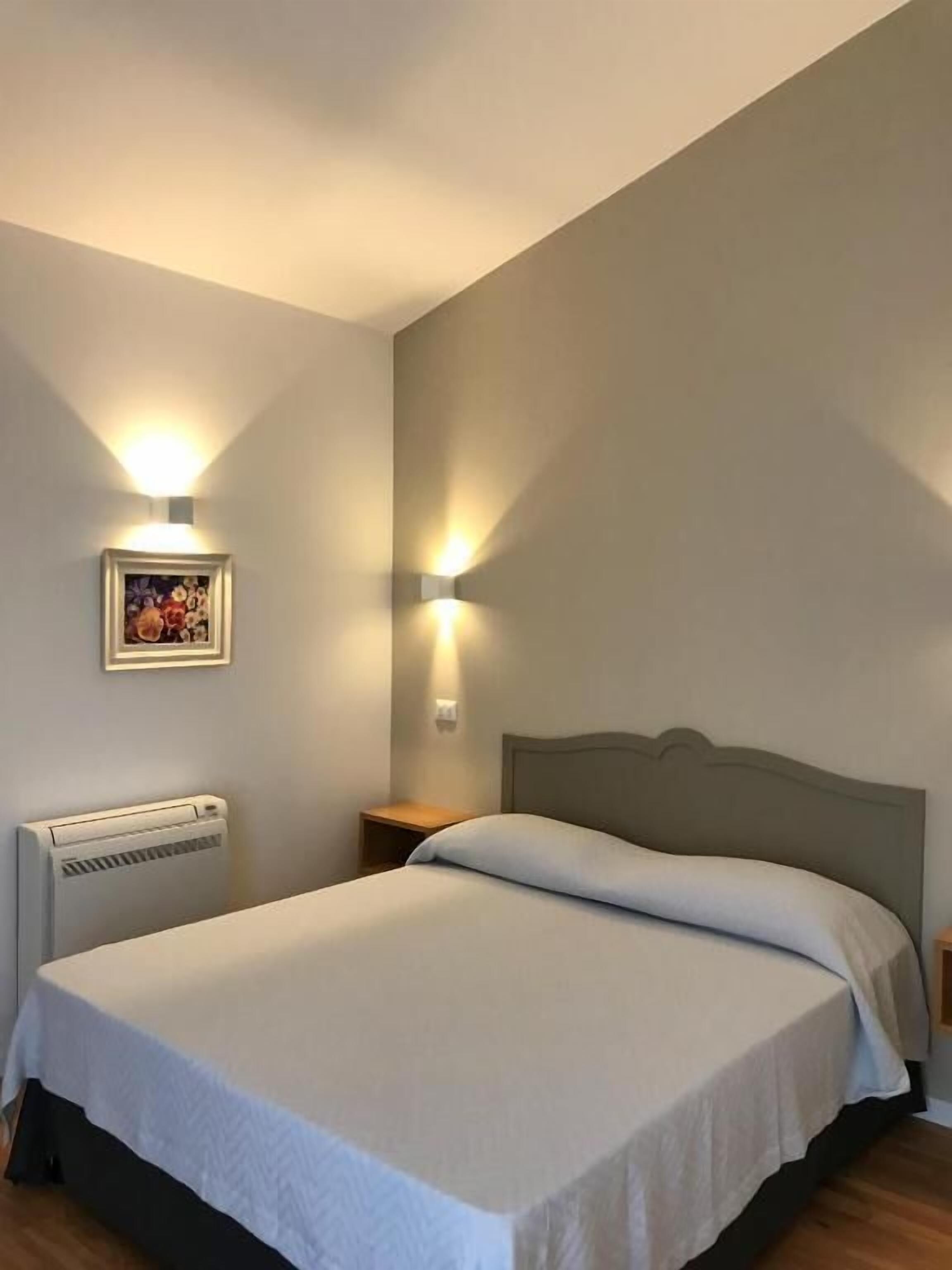 A bedroom with a bed, a radiator, a nightstand, and two wall-mounted lights.