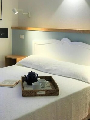 A neatly made bed with a tray of tea set, a book, and a lamp on the nightstand.