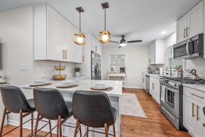 A modern kitchen with white cabinetry, a central island with bar stools, a stove, oven, microwave, and a ceiling fan.
