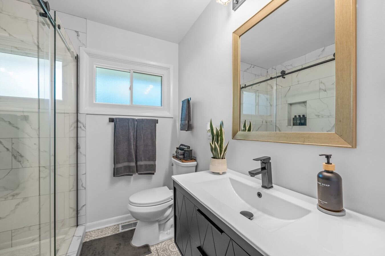Een moderne badkamer met een glazen douchecabine, een toilet, een wastafel met spiegel en een potplant.
