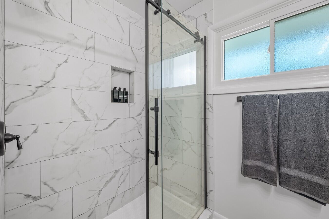 Un bagno con piastrelle in marmo, cabina doccia in vetro e due asciugamani appesi al muro.