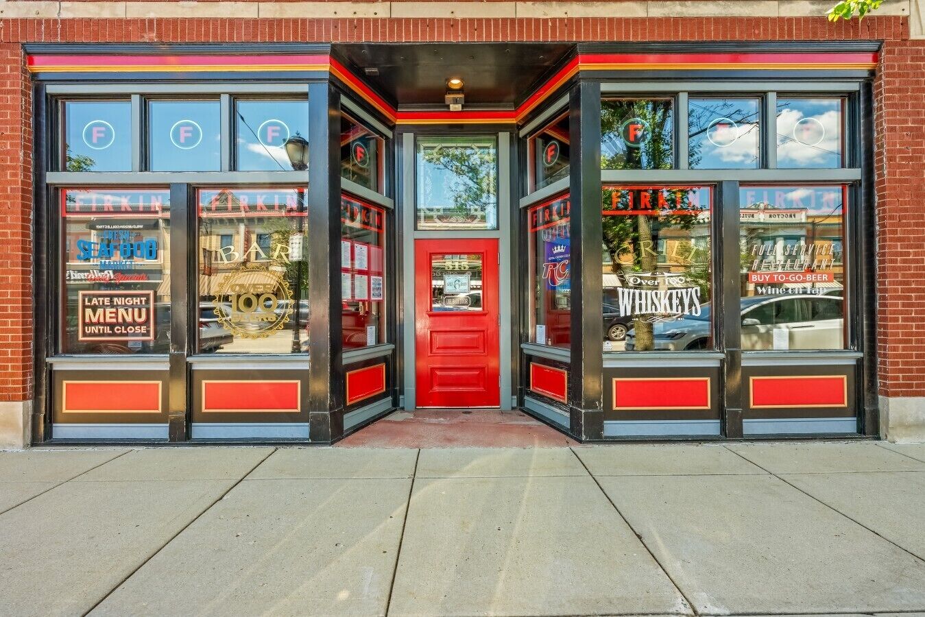 A bar with a red door, large windows, and a sign advertising whiskey.