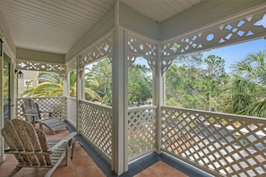 Eine überdachte Veranda mit Holzstühlen, Gittergeländern und Blick auf tropische Vegetation.