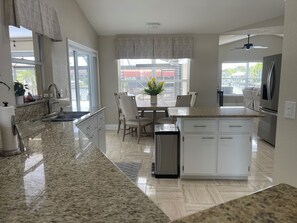 A modern kitchen with granite countertops, a dining area with chairs, a refrigerator, and a ceiling fan. - 3 bedroom home close to resturants,  beach and quick boating access. (Cape Coral)