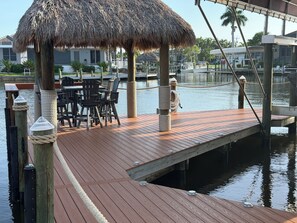 A wooden dock with chairs and a thatched umbrella, a wooden railing, and a body of water. - 3 bedroom home close to resturants,  beach and quick boating access. (Cape Coral)