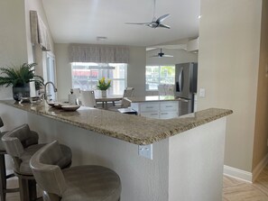 A modern kitchen with a granite countertop, bar stools, a dining table, and a ceiling fan. - 3 bedroom home close to resturants,  beach and quick boating access. (Cape Coral)